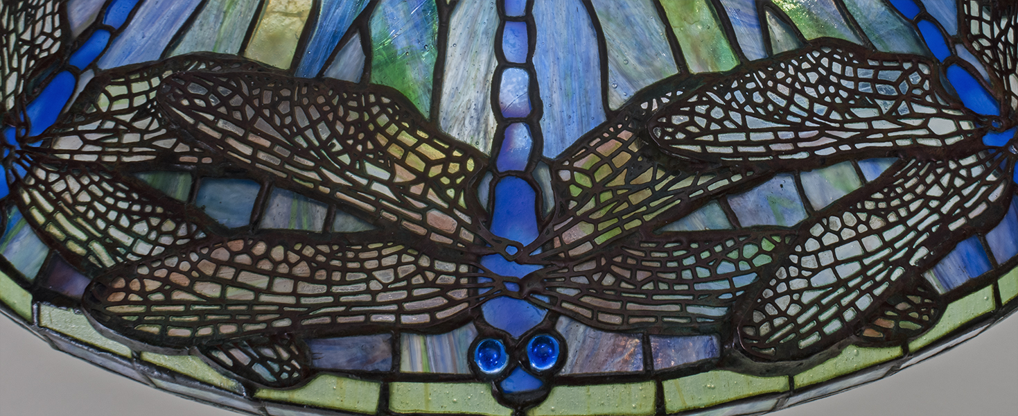 a detail photograph of an authentic tiffany lamp, the conical leaded glass shade depicting dragonflies with filigree-mounted wings