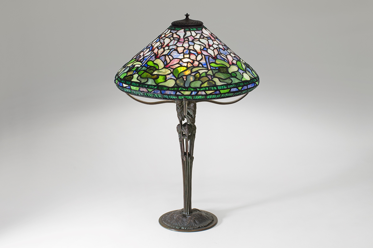 an extremely rare leaded glass tiffany lamp depicting cyclamen flowers in variegated pink and white with green leaves, on a very rare bronze tiffany lamp base, the stem formed by an openwork design of unfurling fern fronds