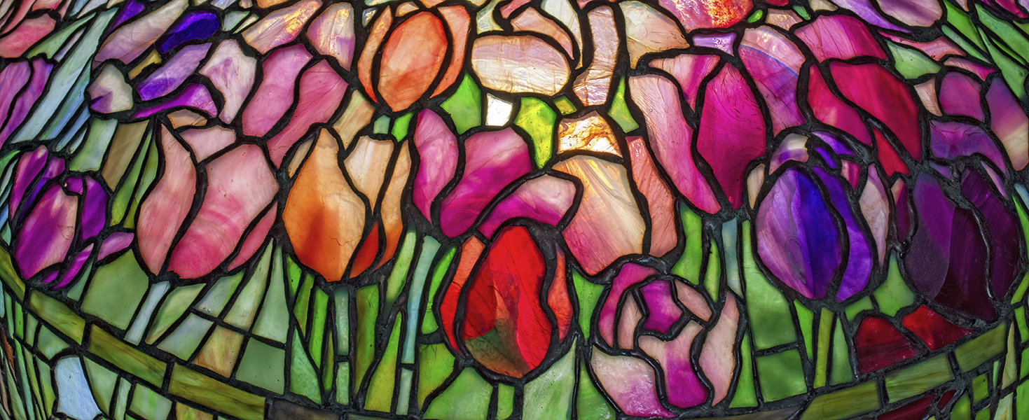 A detail shot of an authentic Tiffany Lamp shade, the leaded glass design depicting a naturalistic field of tulips on variegated opalescent Tiffany Glass in shades of pink, purple and magenta