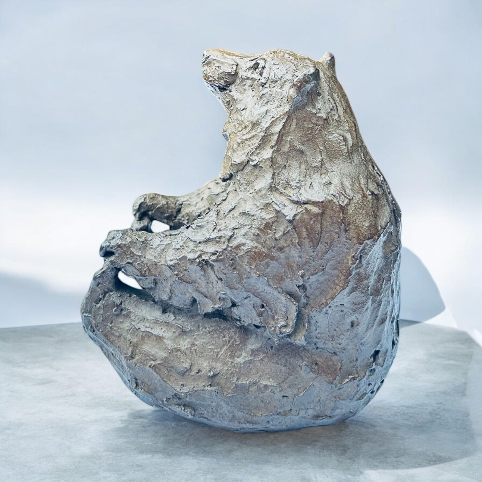 Bear playing with its feet, contemporary animal bronze sculpture by Bast, playful figurative artwork with expressive textured surface, collectible sculpture for indoor or outdoor display