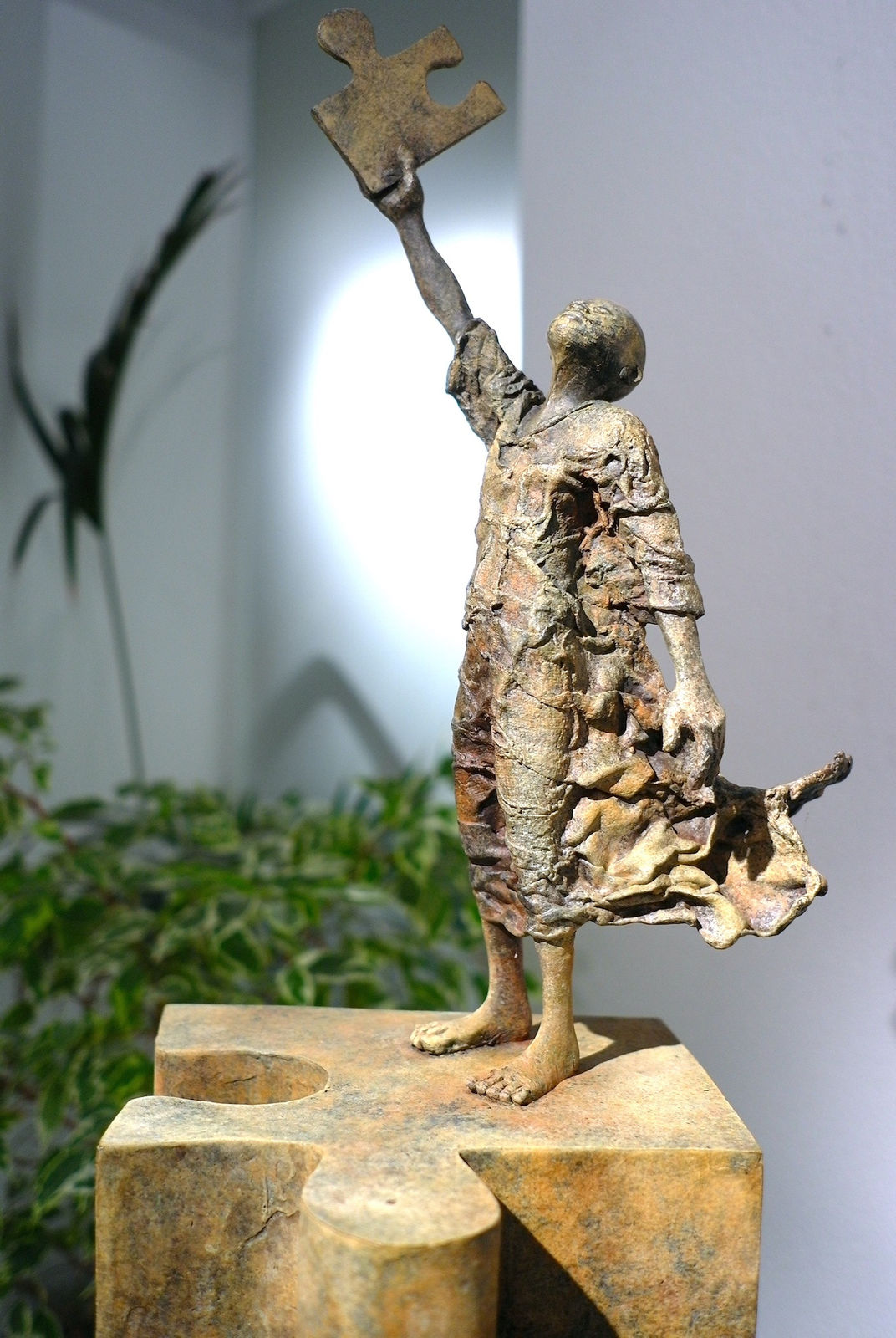 Sculpture en bronze “Eureka” de Lieven D’Haese, représentant une figure debout sur une pièce de puzzle monumentale, levant un fragment vers le ciel dans un geste de découverte.