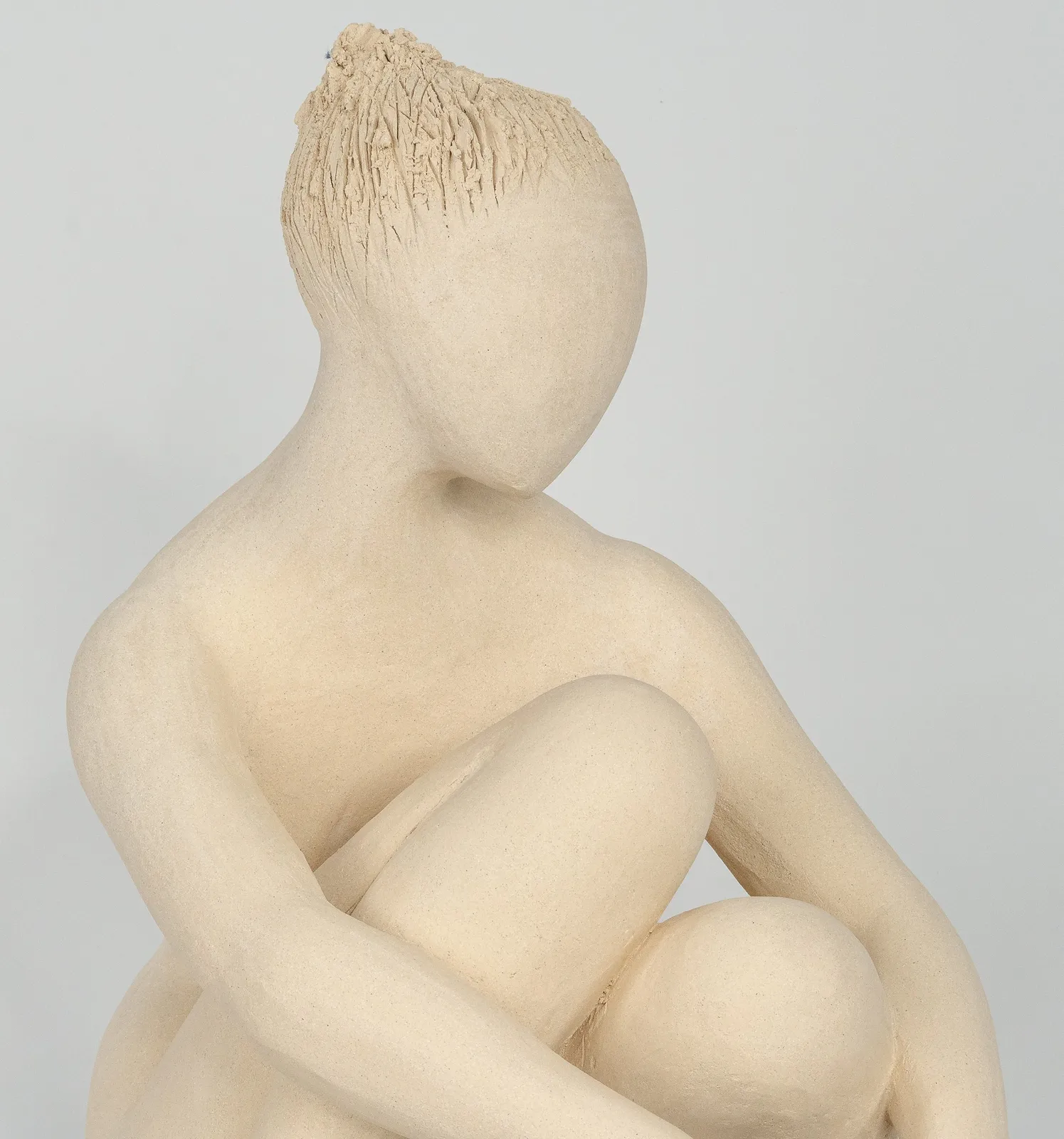 Seated white ceramic figure is looking over her left shoulder with arms draped around her knees which are tucked together.