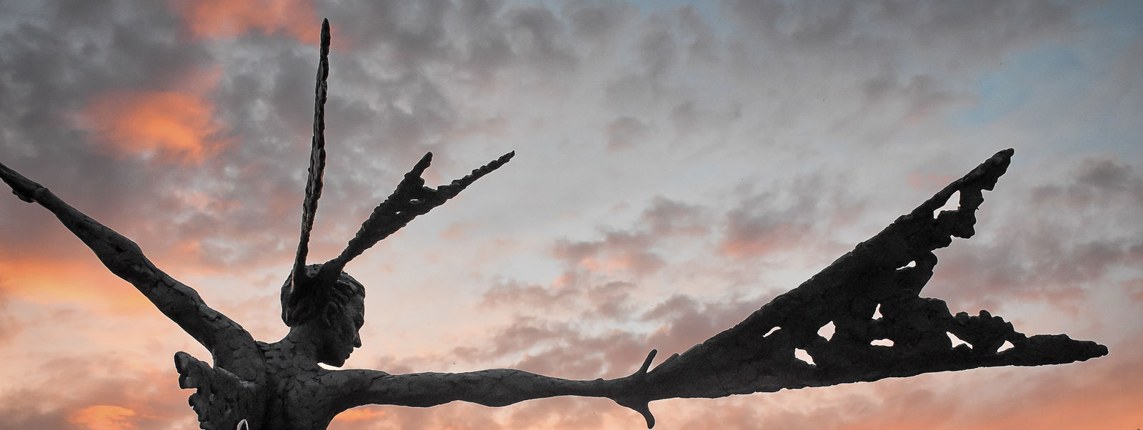 A monumental bronze sculpture of a winged female by Nicola Godden stands in front of a sunset at a Dorset sculpture park, Sculpture by the Lakes