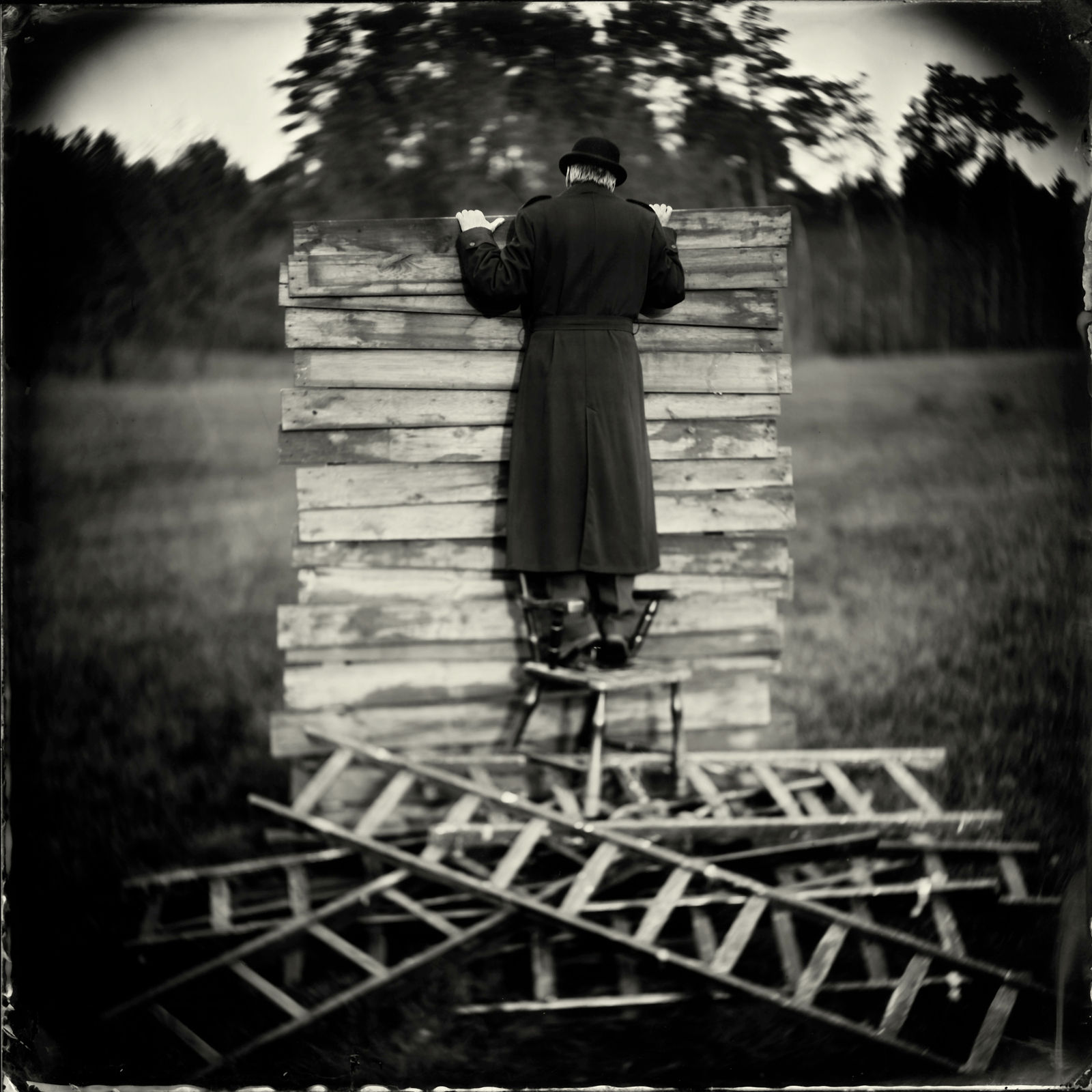 A man perches on a chair peering over a wooden wall