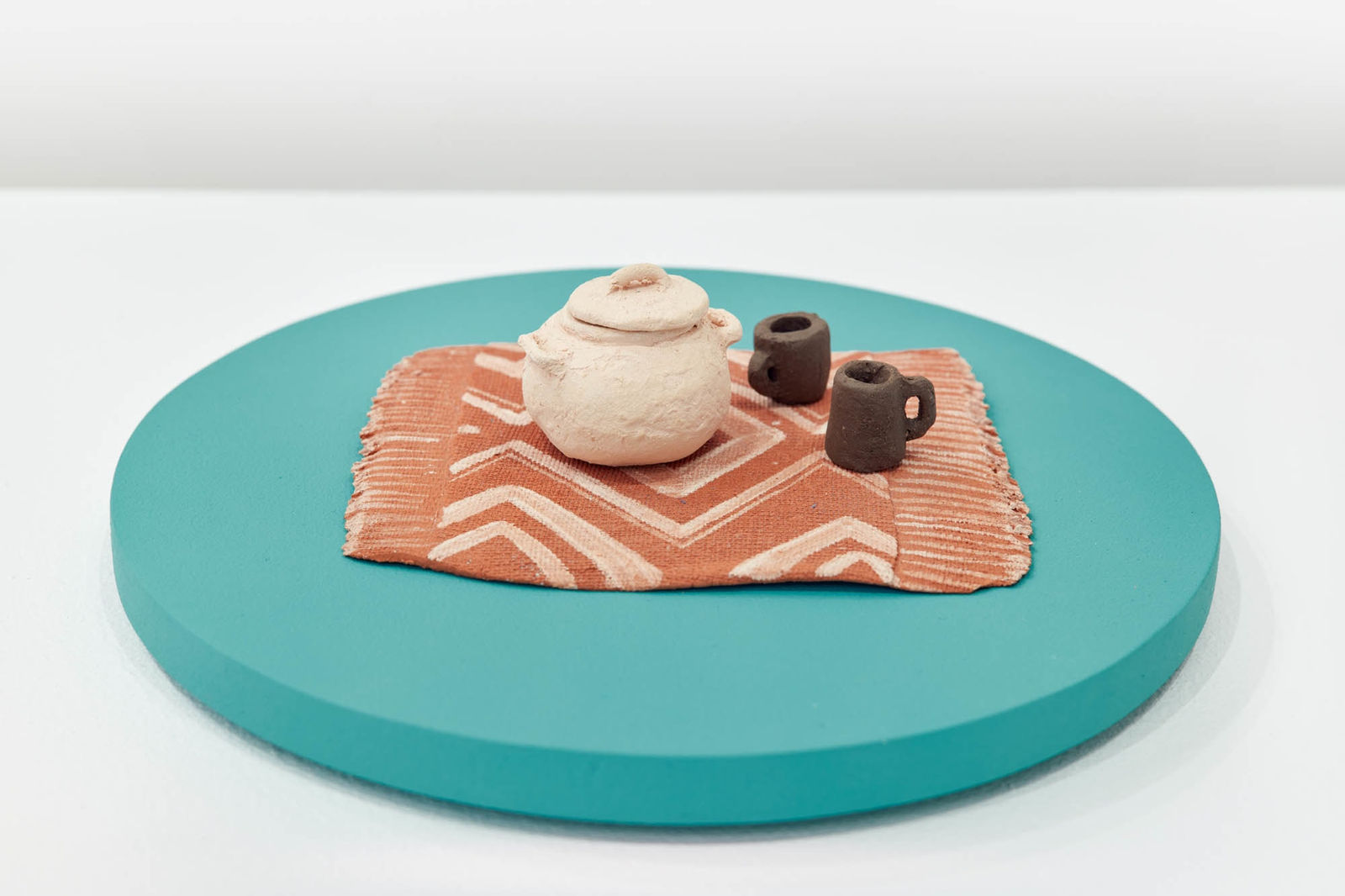 a small model of ceramic vessels atop a geometrically patterned rug. The model is sitting atop a turquoise platform