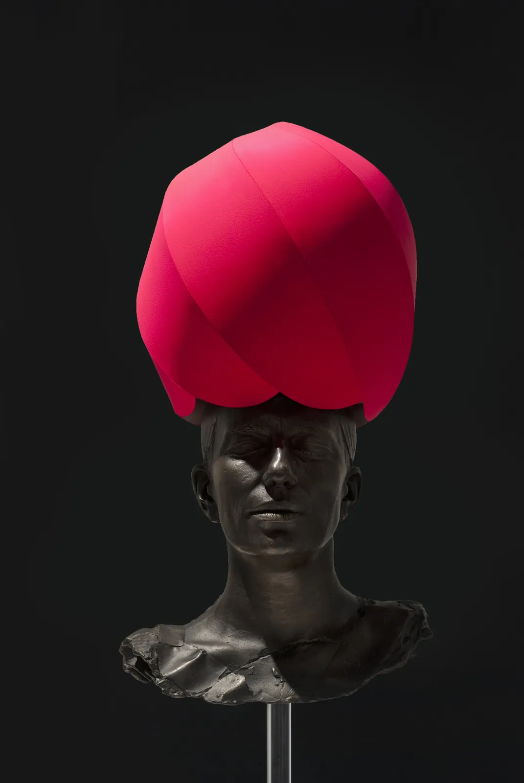 A bronze sculpture of female head, against a black backdrop, with a red head covering.