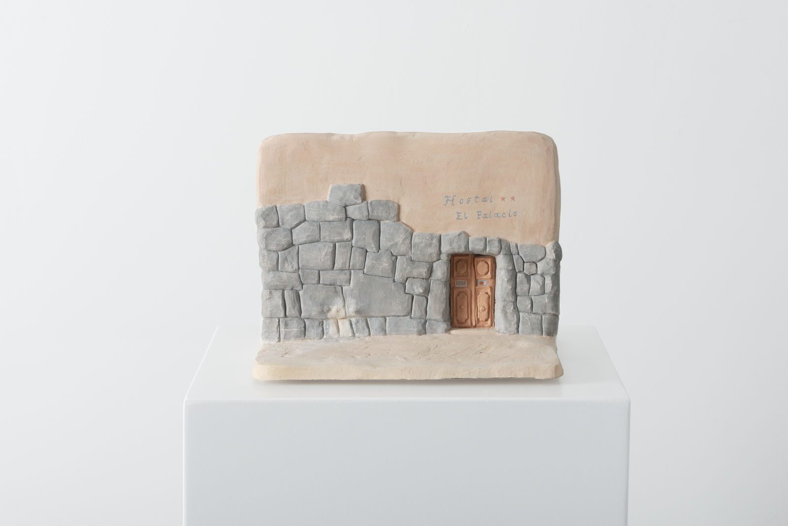 small ceramic piece modeling a wall and floor -- on one side of the wall is a door through the Peruvian twelve-angled-stone wall, above which is text reading 