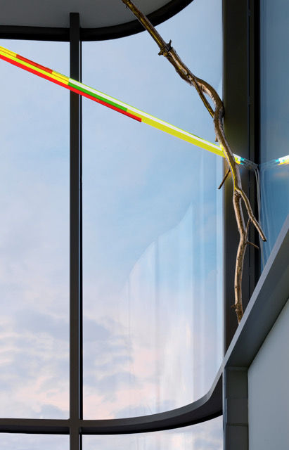 Bronze, coloured glass, and neon hanging next to a window through which can be seen a blue sky.