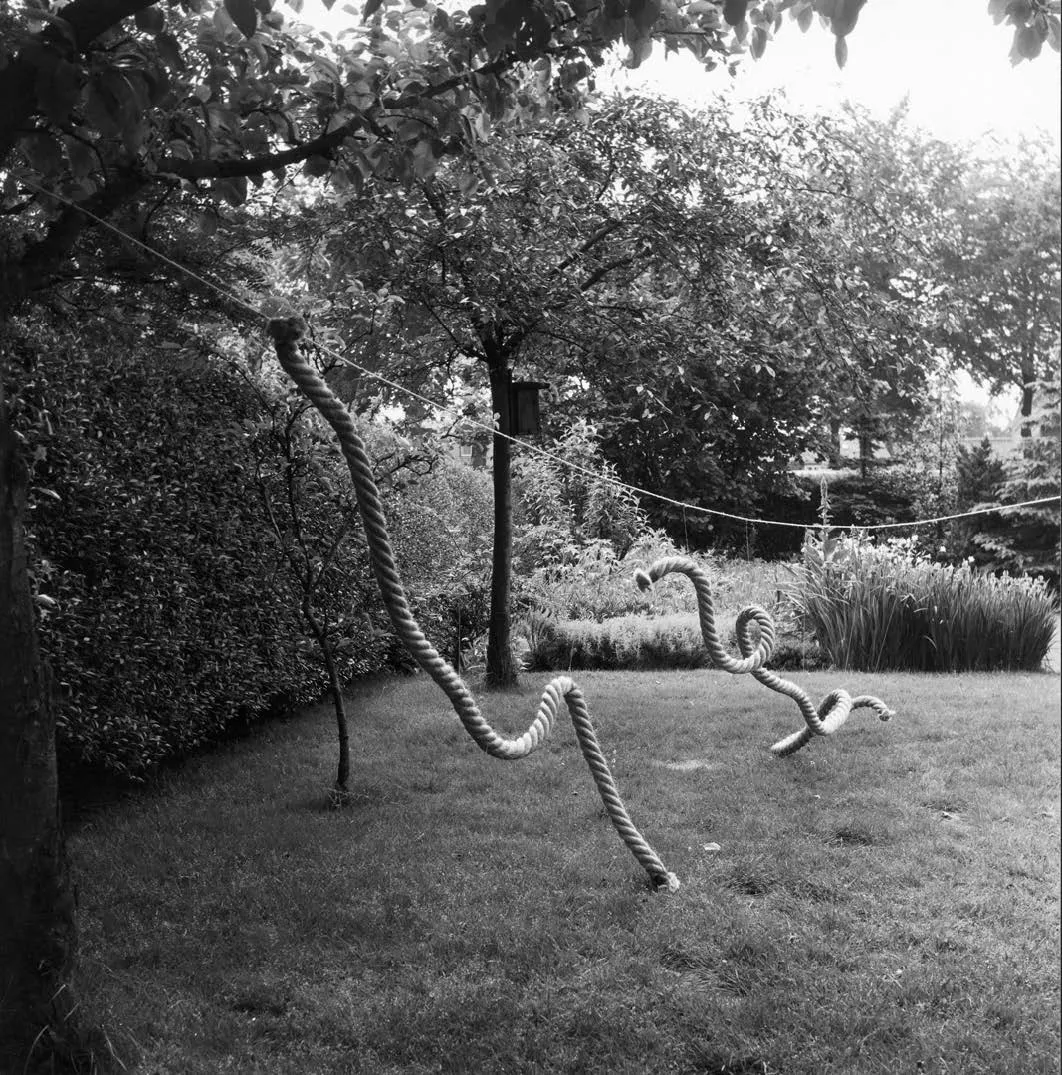 A sculpture of pieces of rope hanging from a string suspended over the ground outdoors.