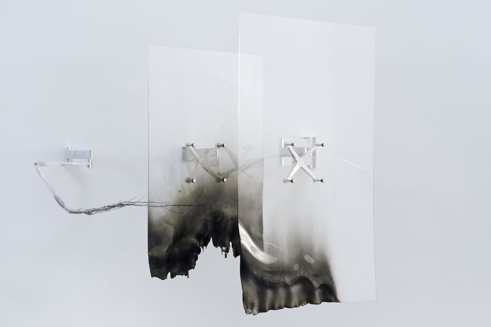 An image of two burned acrylic sheets attached to a white wall by aluminum spider brackets and rods.