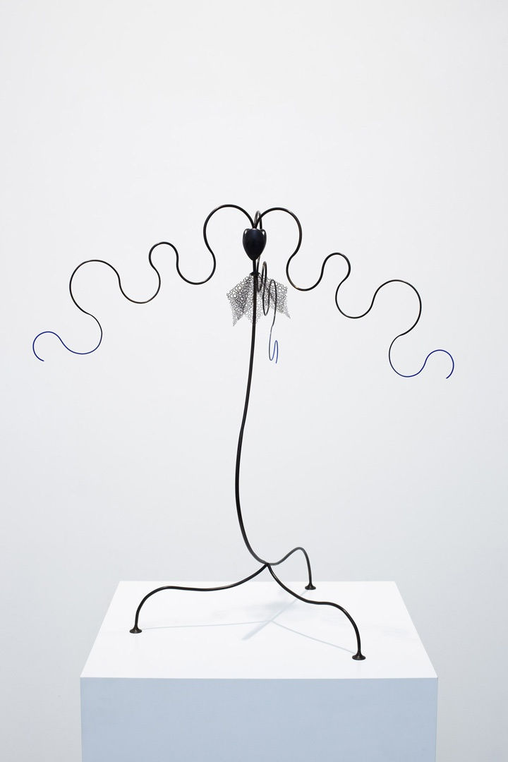 An acrylic and brass sculpture that resembles a candlestick with three legs and branches spiraling from the top.