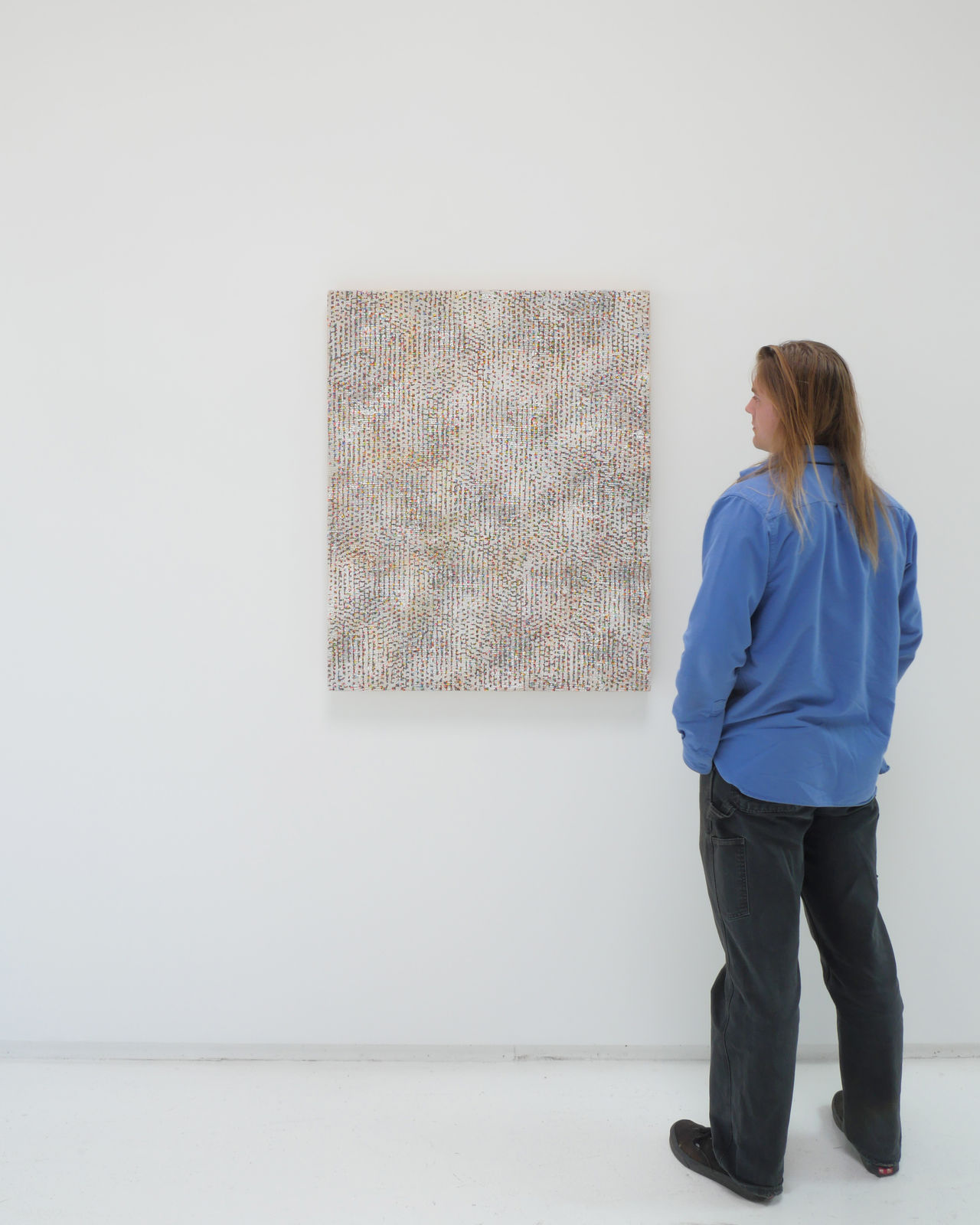 A man stands to the right and faces a multicolored abstract painting.