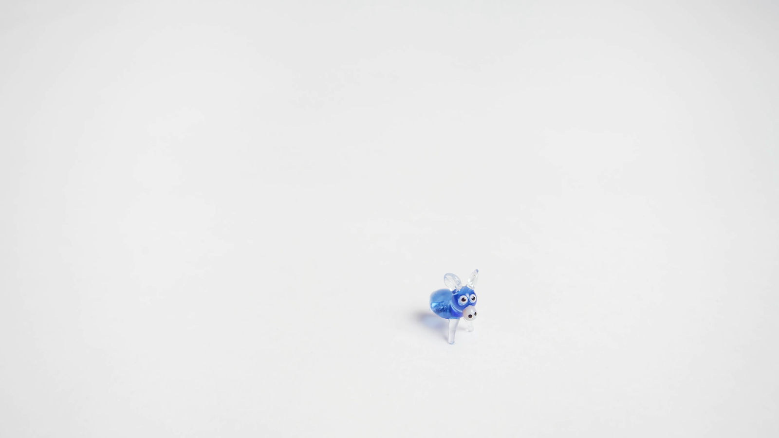 still from video shows a small blue and clear glass figurine of a four legged animal on white background