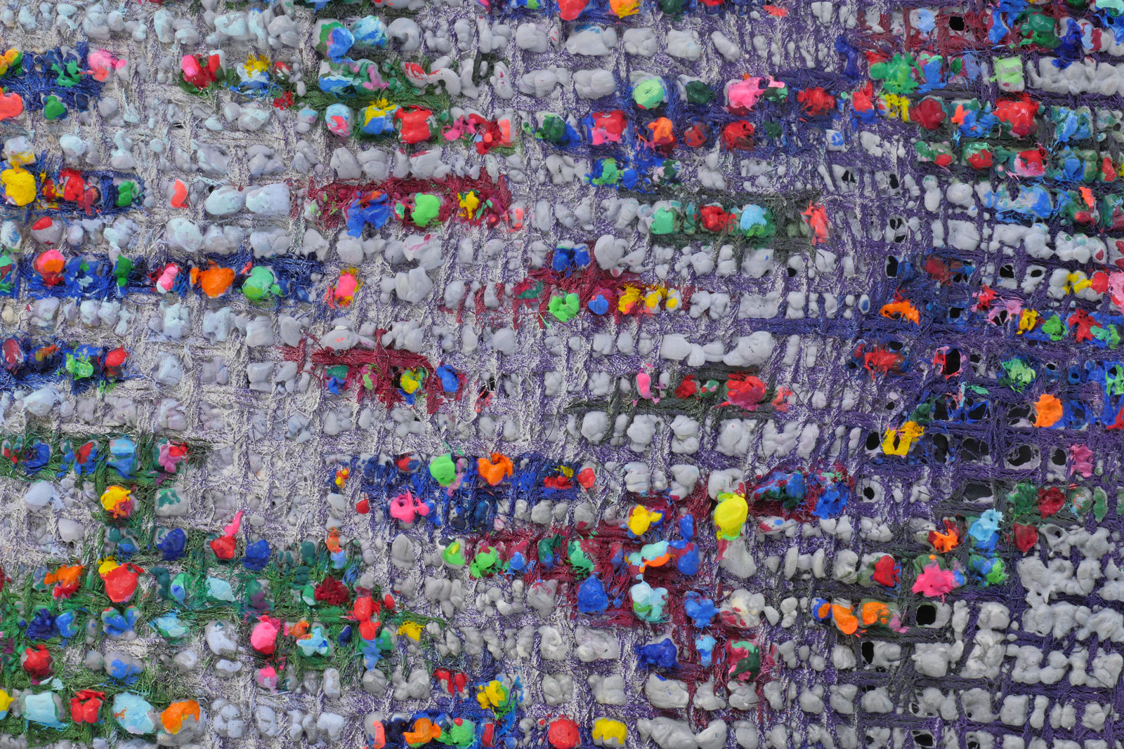 Detail; multicolored paint protrudes through multicolored canvas.