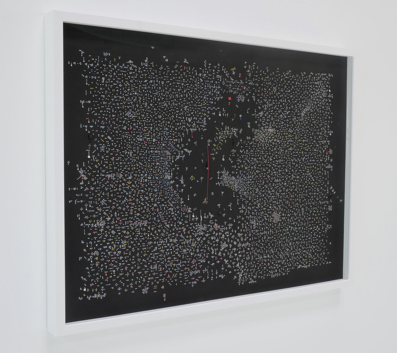 Side view of a framed black, horizontal rectangle with millions of white dots, hanging on a white wall.