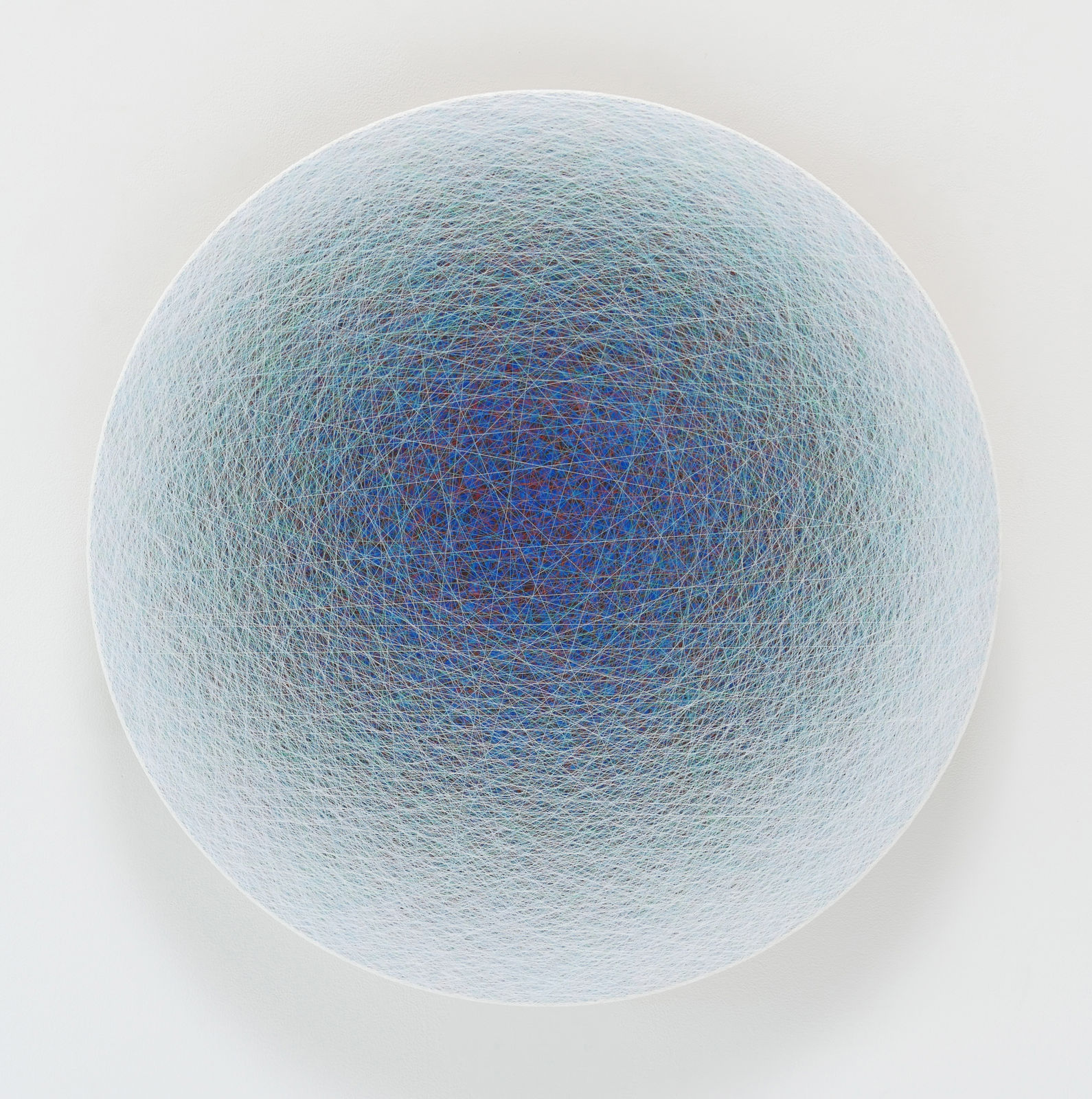 Layers of multi-colored threads strung across a round wooden and plaster panel create the effect of a tight dark blue center that fades to pastel blue on the outer border