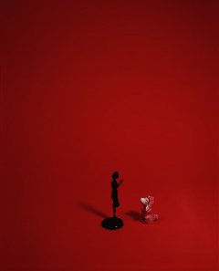 Duraflex print of a digital photograph which depicts a short pink poodle figurine looking up towards a taller black figurine. The two objects are surrounded by a red background with a black vignette