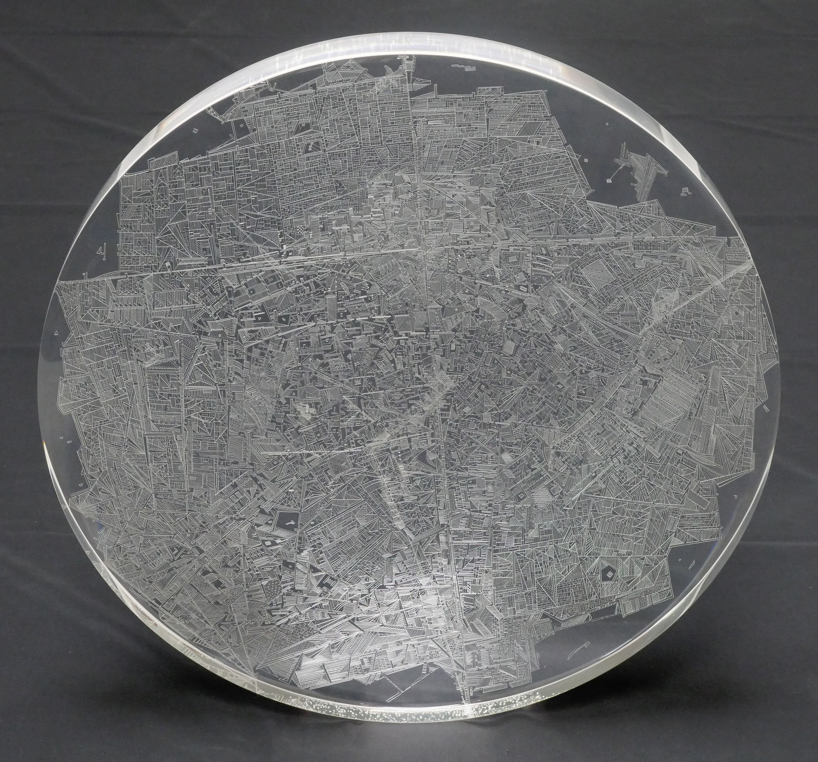 Front view of a clear convex disk with etchings set on a dark grey background.