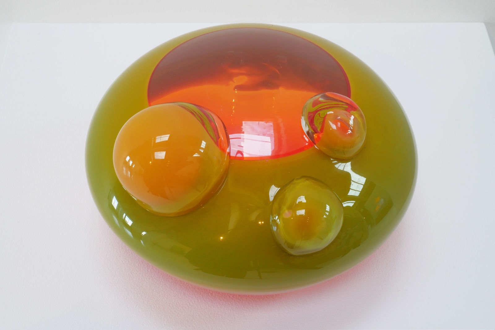 Top view of the sculpture with a clear glass middle, through which a florescent orange glow is visible.