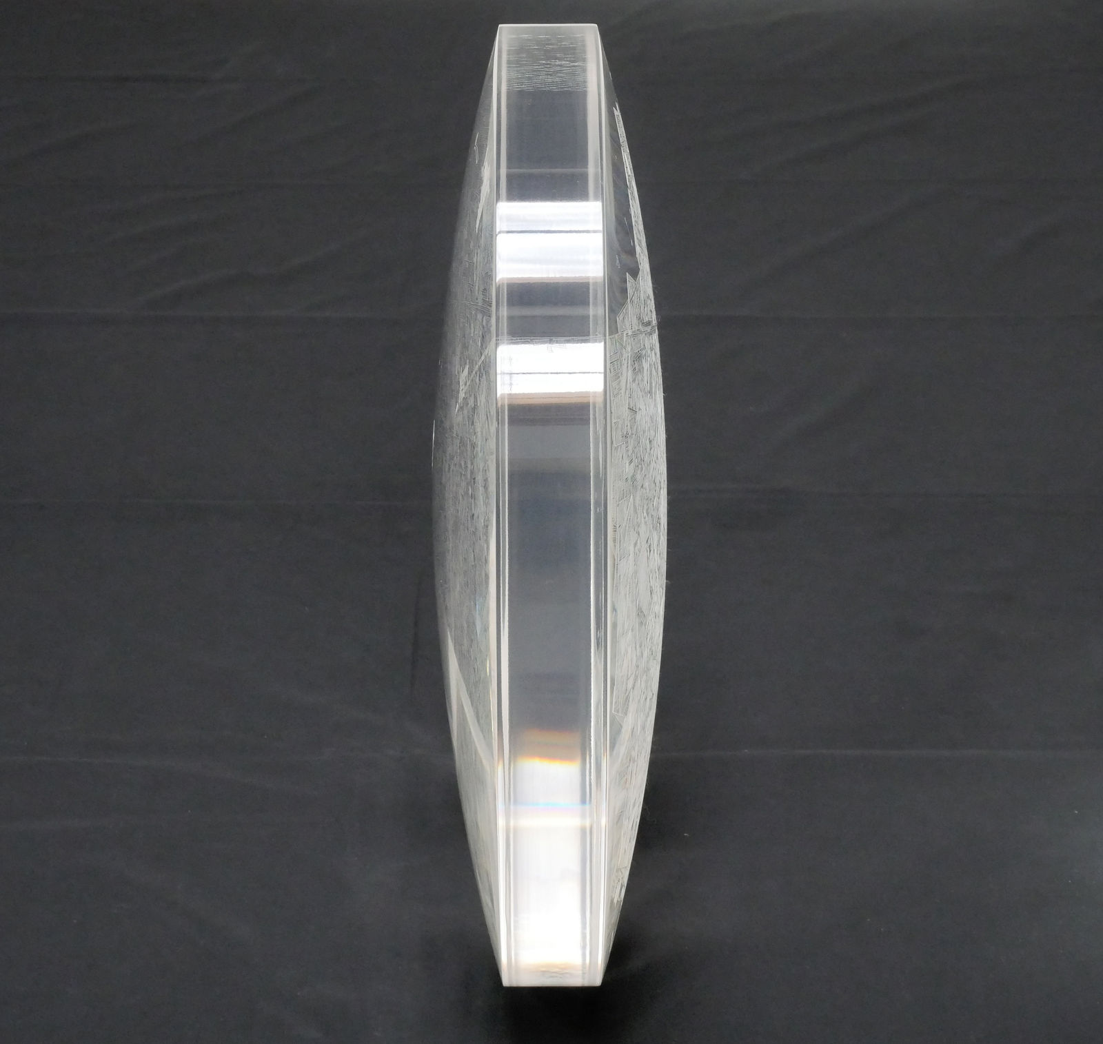 Side view of a clear convex disk with etchings on both sides set against a dark grey background.