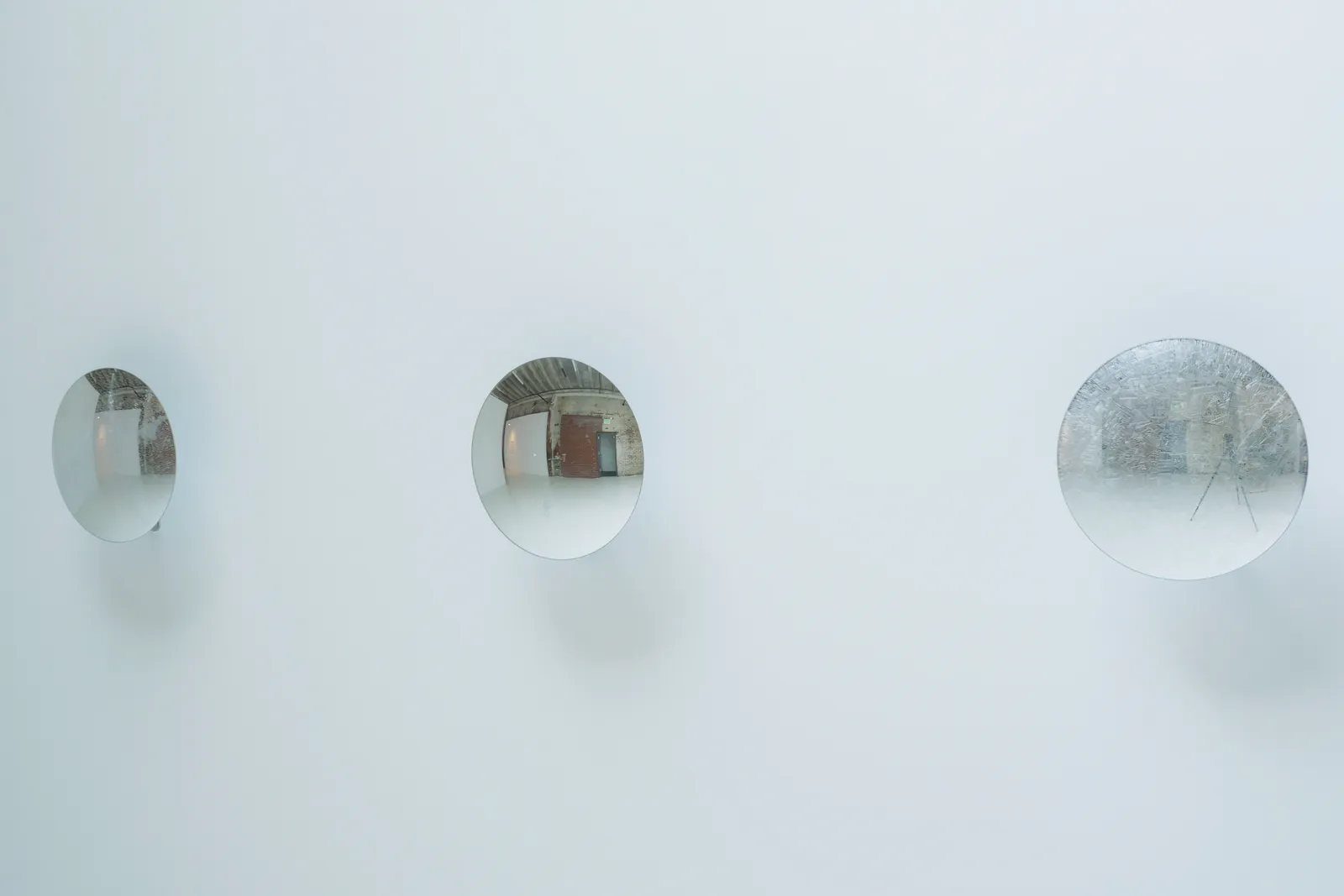 Side angled view of three reflective disks mounted in a row on a white wall.