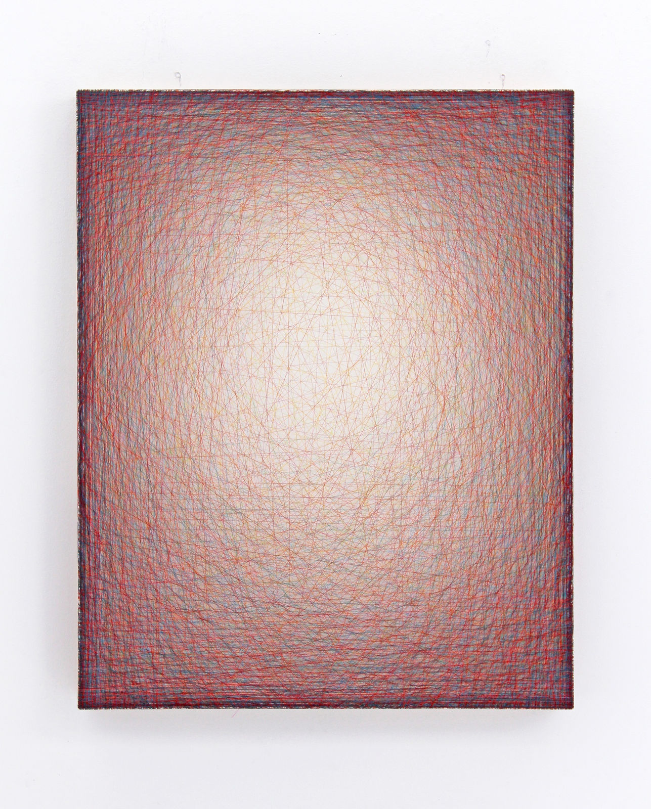 Layers of multi-colored threads strung across a rectangular wooden and plaster panel create the effect of a small glowing white center that is enclosed by a pink and red border