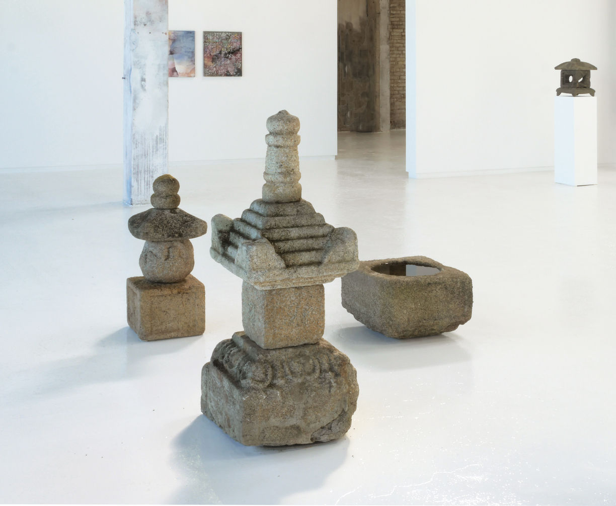 Assortment of Japanese stone sculptures in gallery with colorful paintings on back wall.