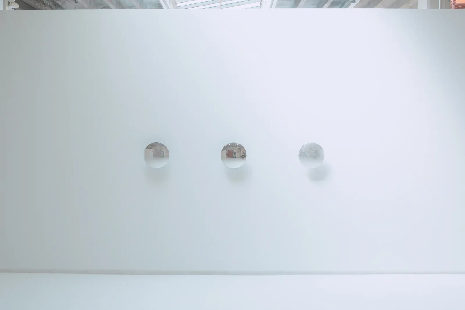 Distanced view of three reflective disks mounted in a row on a white wall.