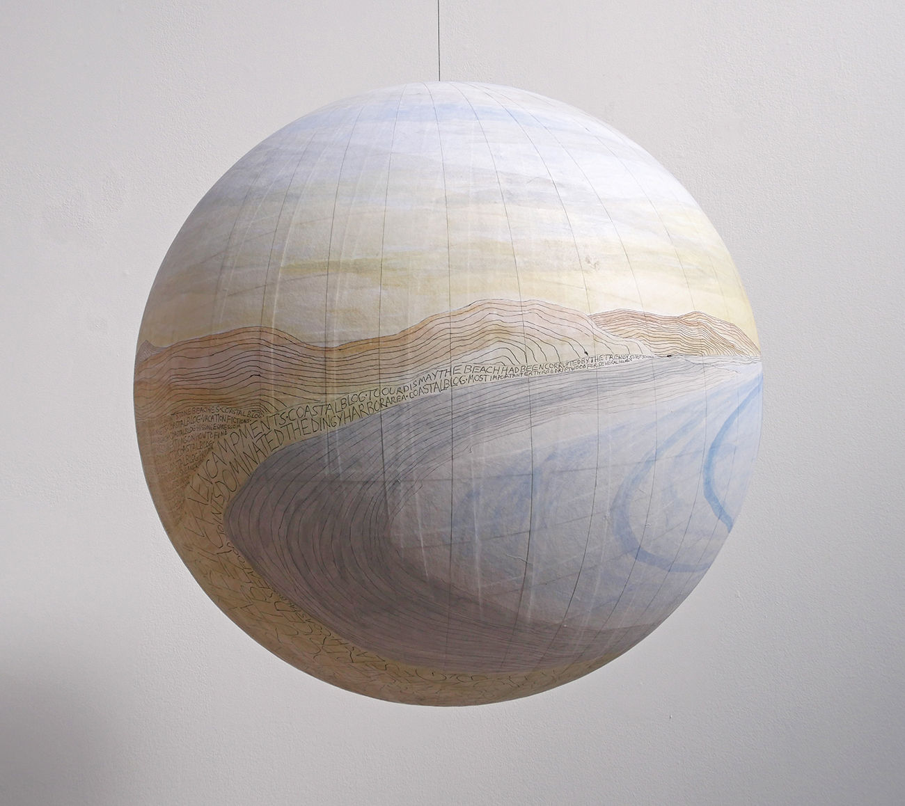 Ballpoint pen drawing with washes of blue yellow and orange acrylic create a hilly beach landscape on paper which is pasted onto a large fiberglass hanging globe. Throughout most of the sandy landscape various thoughts are scribbled down in all caps
