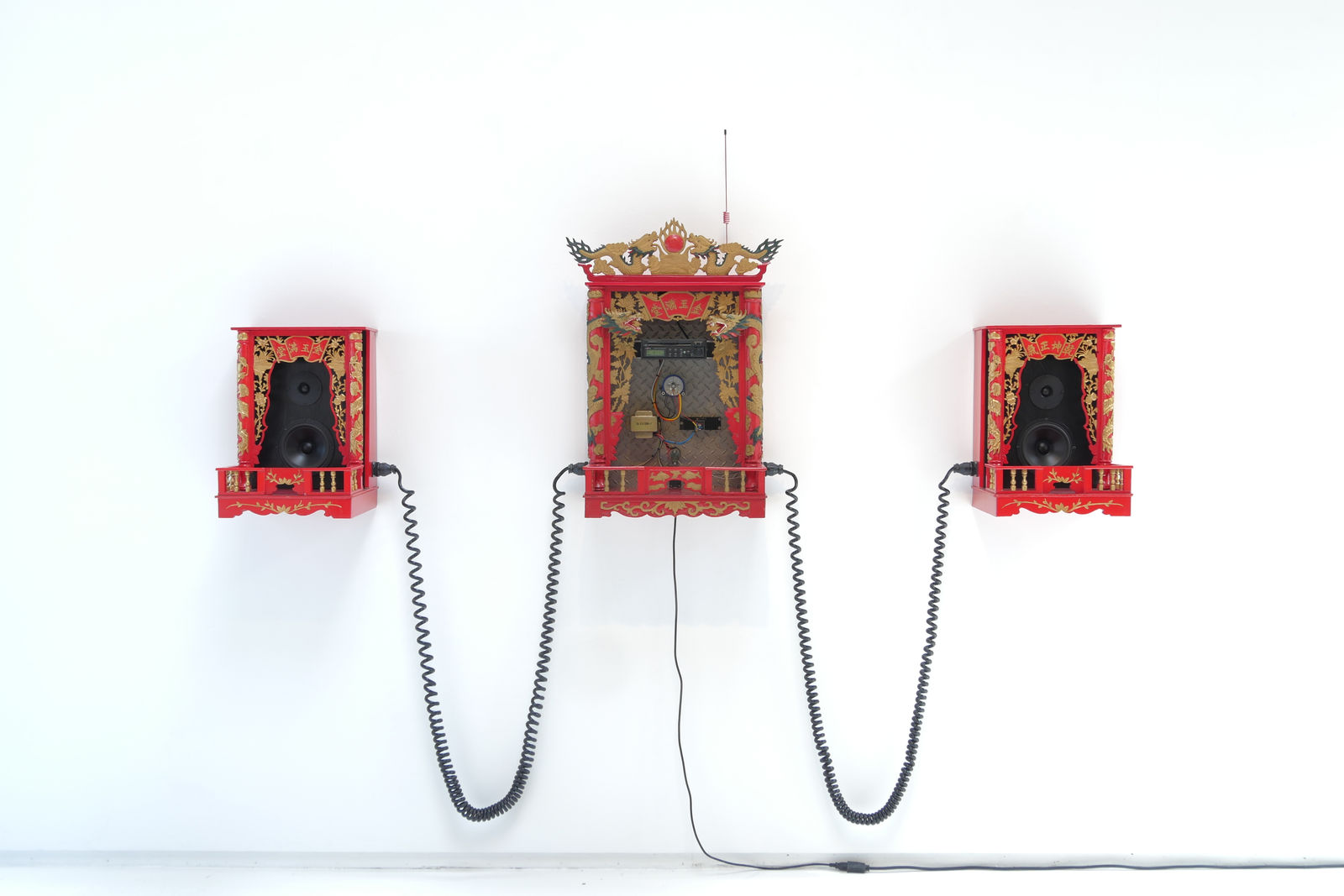 Thee red Chinese altar boxes with speakers on sides and stereo incenter, connected by coiled black wire.