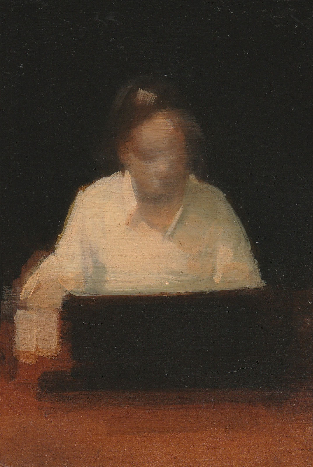 Woman sits at a wood table with an unidentifiable dark brown object against a black background.