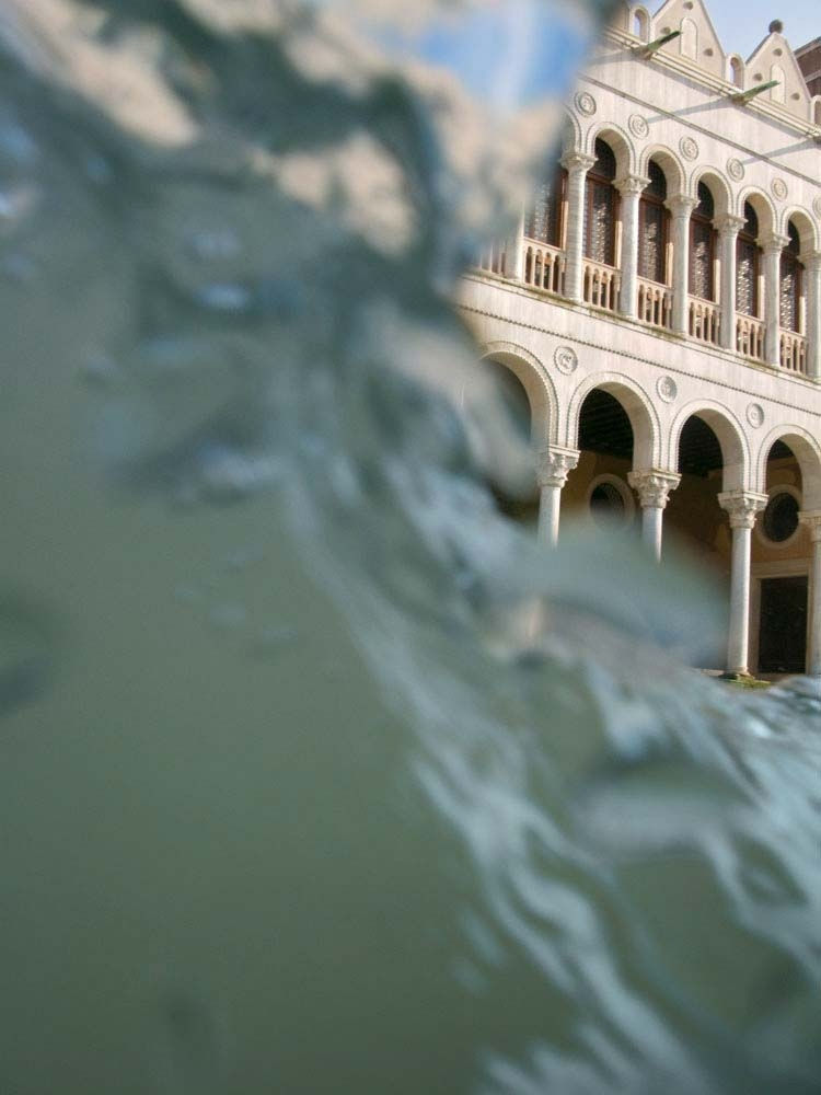 wave of water on left side of frame, with white sunshine lit palazzo on top right side, perfect Venetian arches, by Mona Kuhn