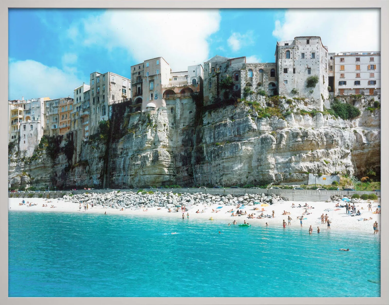 Aquamarine sea with beachgoers, below old buildings built on cliffs, by Massimo Vitali