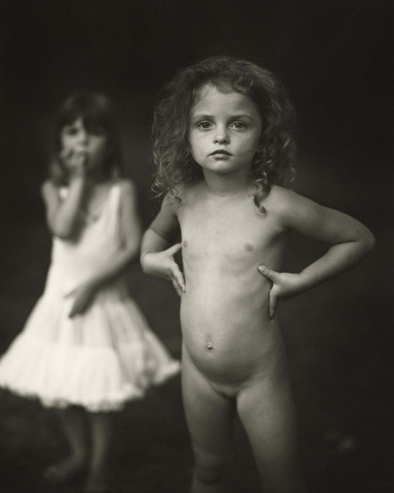 Virginia at 4 by Sally Mann from Immediate Family series, black and white portrait photograph of a young girl standing confidently with another child blurred in the background
