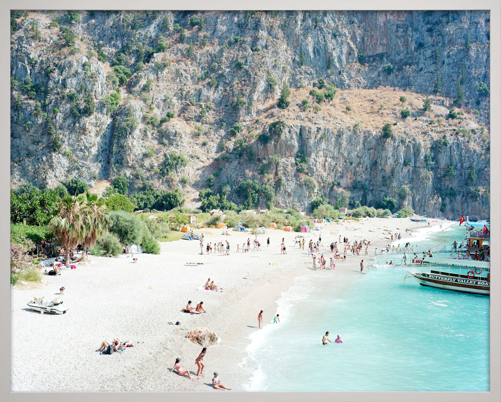 Beachgoers relaxing by the ocean with cliffs in background in Butterfly Valley, Turkey, by Massimo Vitali