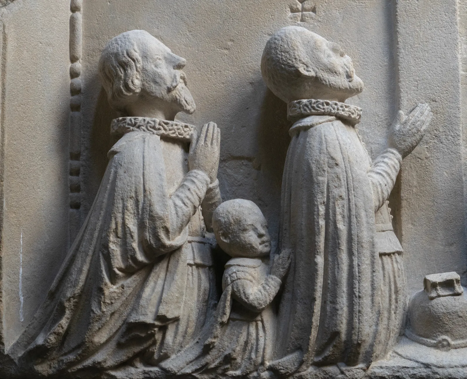 Detail of a fragment of an epitaph from c. 1600, depicting a family in prayer. On the left, two bearded men and a small child kneel, facing right with their hands clasped. On the right, four women kneel, facing left in a similar prayerful pose. All figures are dressed in period clothing with prominent ruffled collars. La Gabrielle Fine Arts SA, Geneva.
