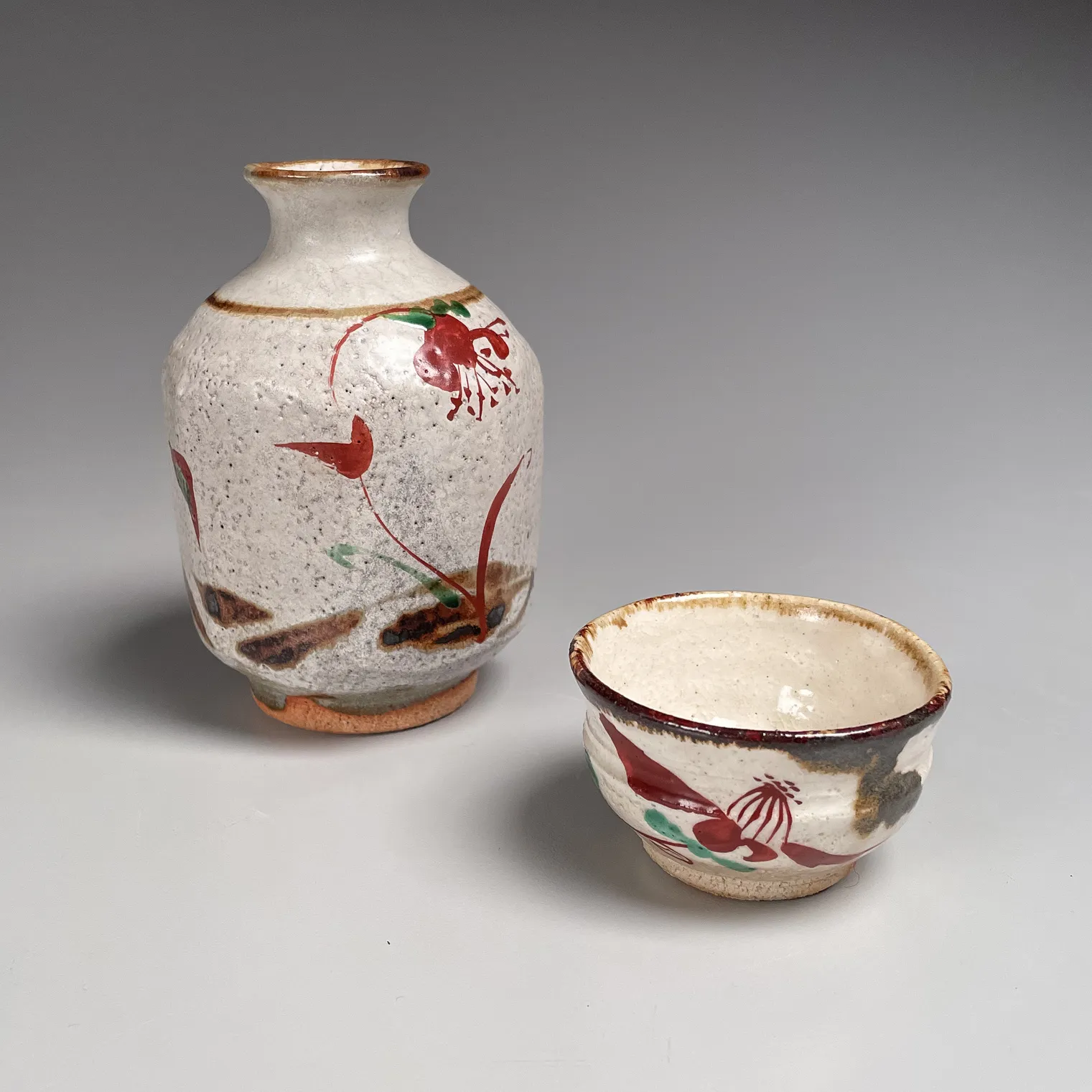 FUJIMOTO YOSHIMICHI (NŌDŌ), Stoneware tokkuri (sake flask) and guinomi (sake cup) with red and green floral patterning, ca. 1975