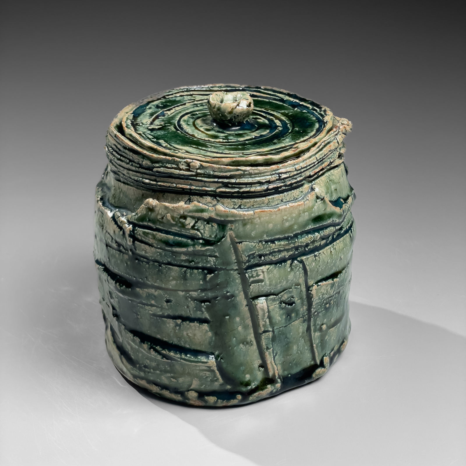 OKABE MINEO, Oribe-glazed round waterjar with carved banding and matching circular cover, ca. 1964