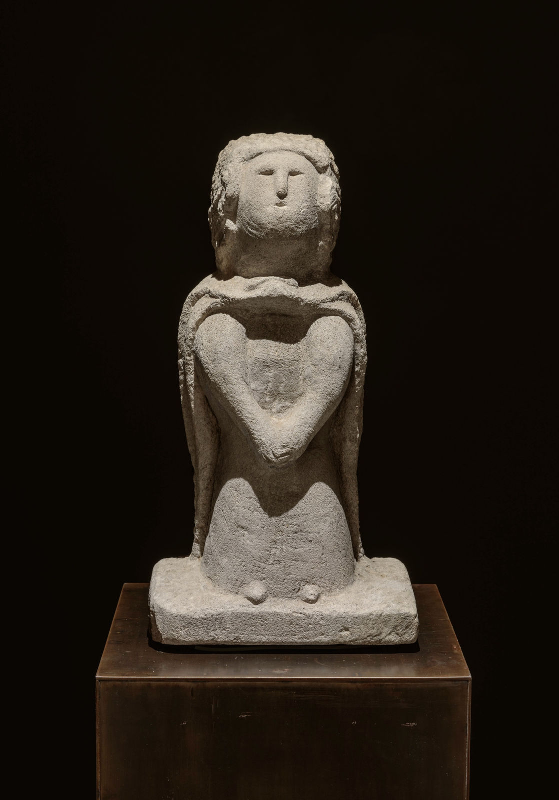 Simple sculpture of a person standing with hands together, wearing a cloak.