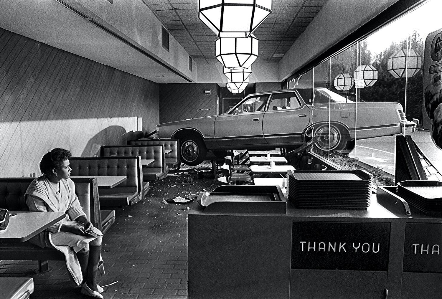 A black and white photograph by Spencer Ainsley showing a woman, who was unhurt, sitting in a Hardee's Restaurant booth in Lenoir, North Carolina after accidentally driving her car through a window before ordering breakfast.