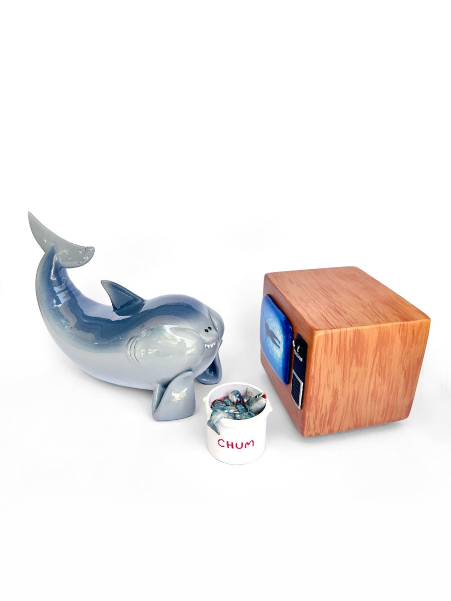 sculpture of a ceramic shark watching a tv screen with a bucket next to it