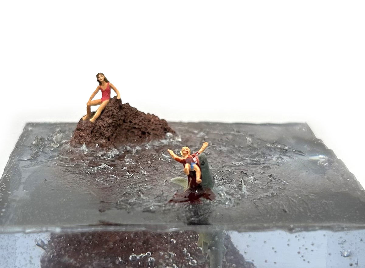 sculpture of a woman on a rock and another woman being eaten by a shark in the water