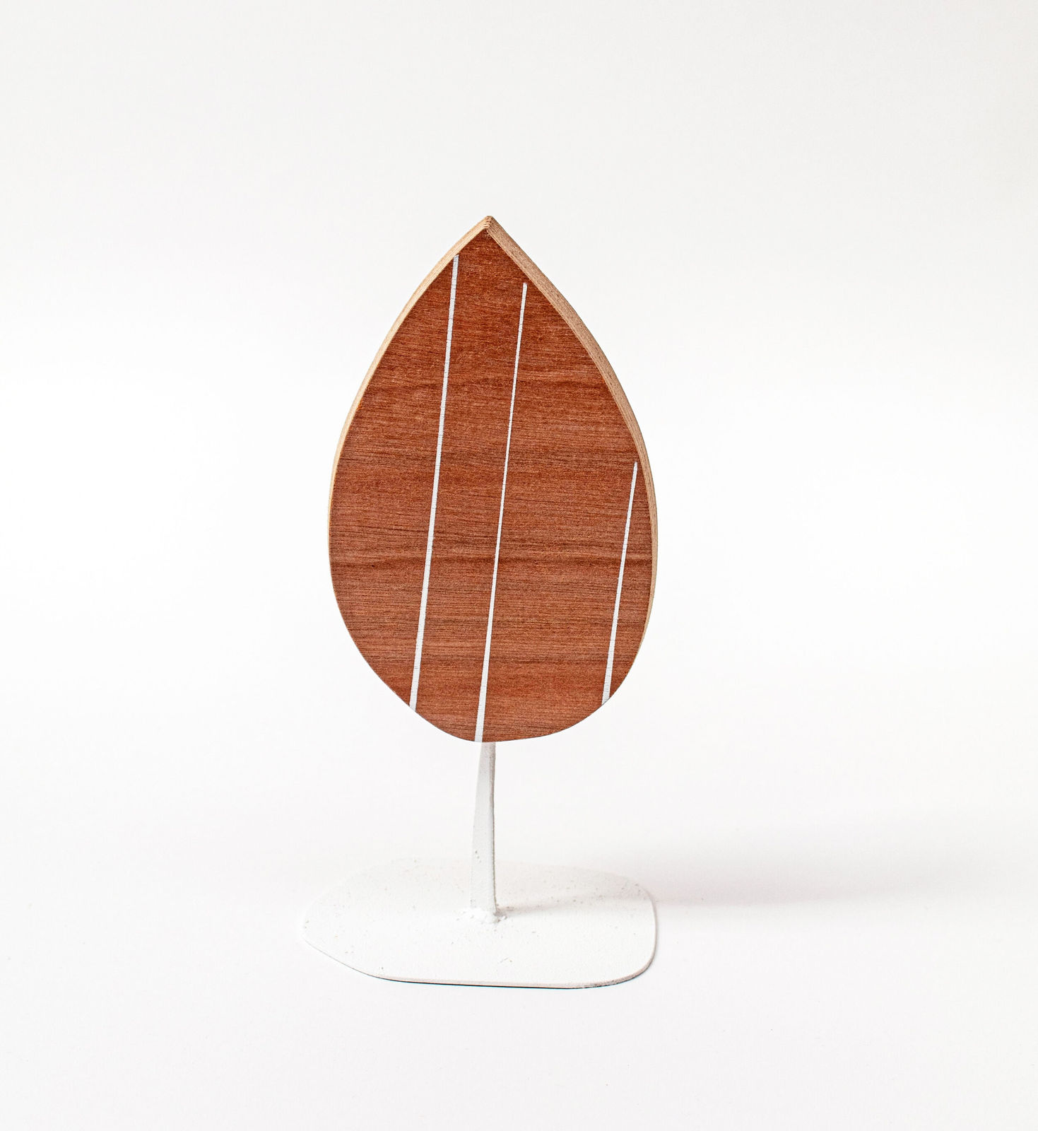 Wooden sculpture of a tear drop shaped piece of wood with three white stripes vertically across it on a white steal stand