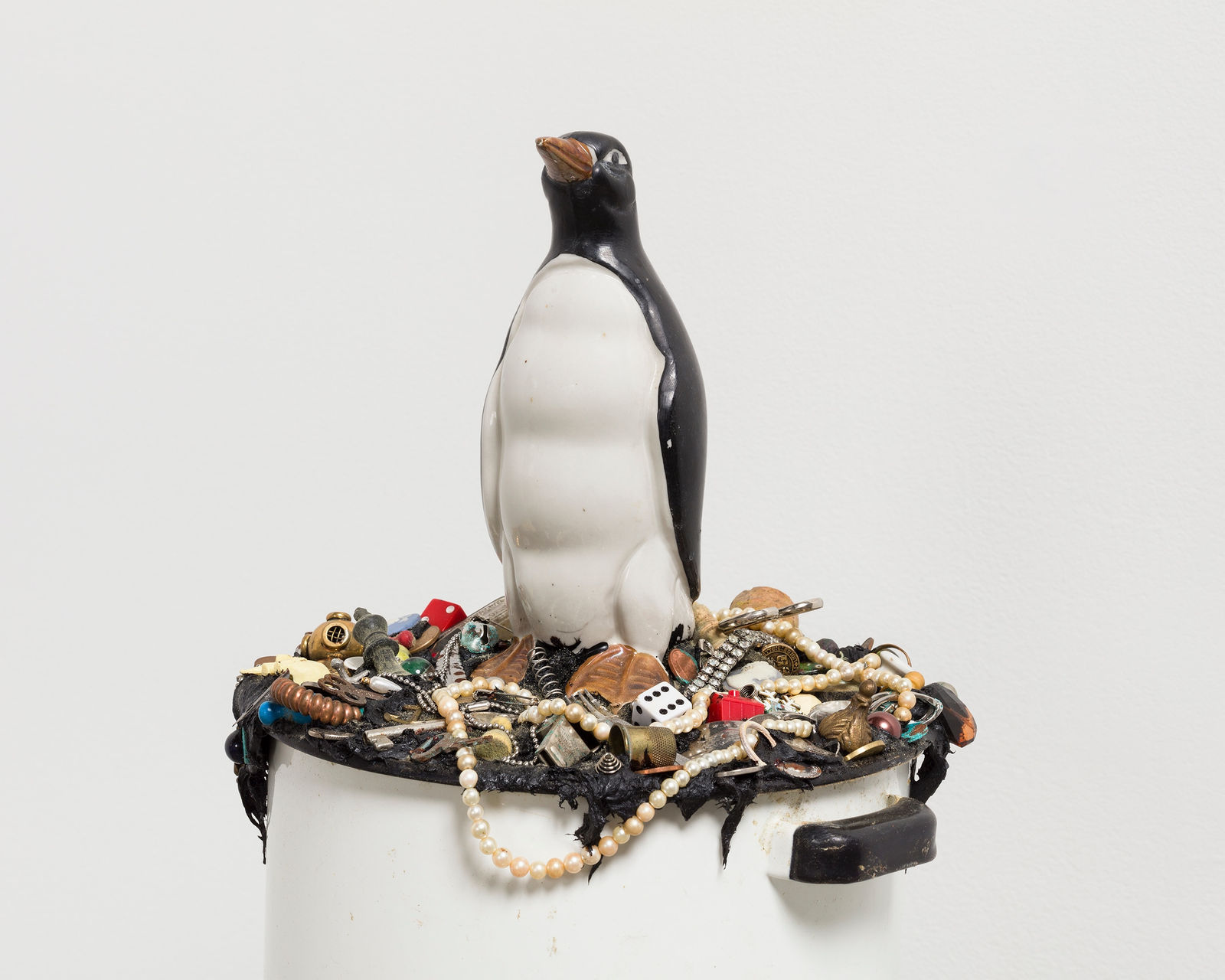 Cropped view of penguin sitting atop of a white pot filled with knick knacks