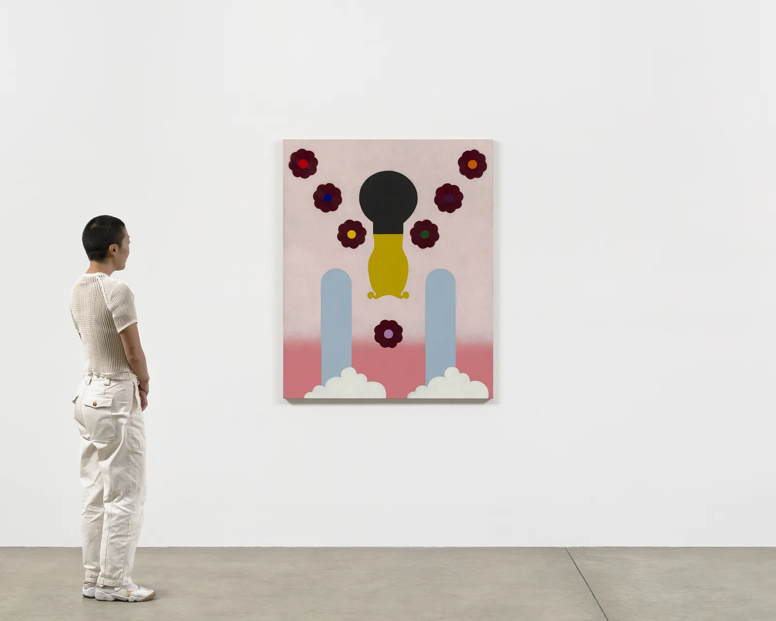 Scale of figure near colorful graphic painting with flowers and clouds against white wall