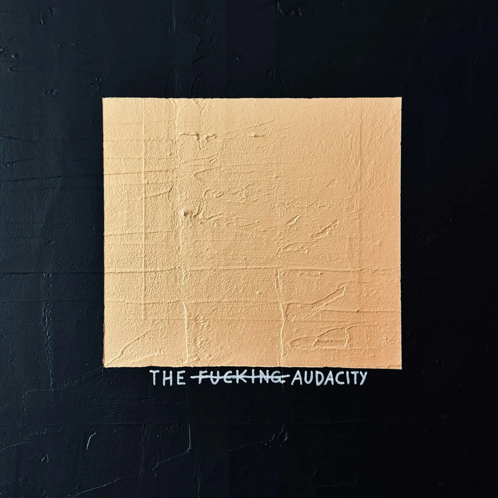 A high-contrast close-up of the textured gold square, revealing raw, tactile ridges and the subtle hand-painted text 