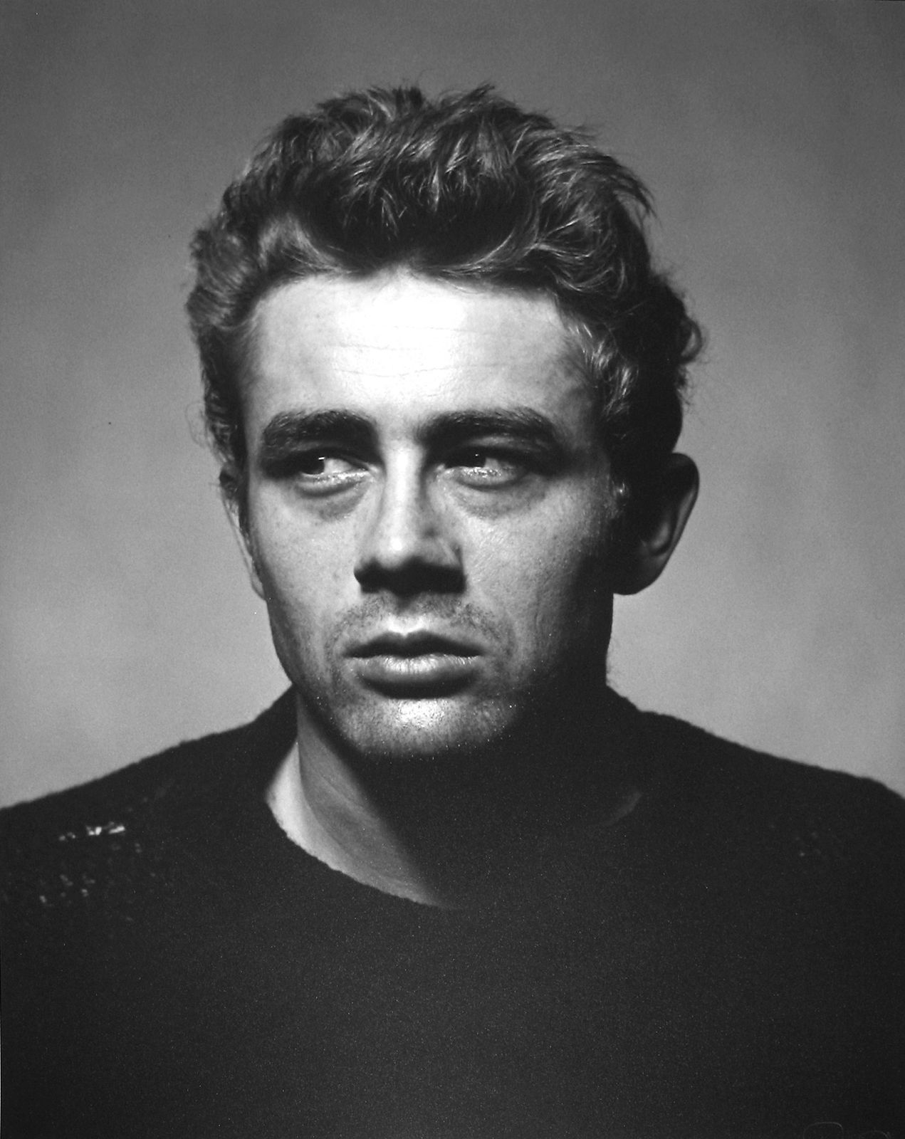 Black and white portrait photograph of James Dean with a sideways glance in a black sweater