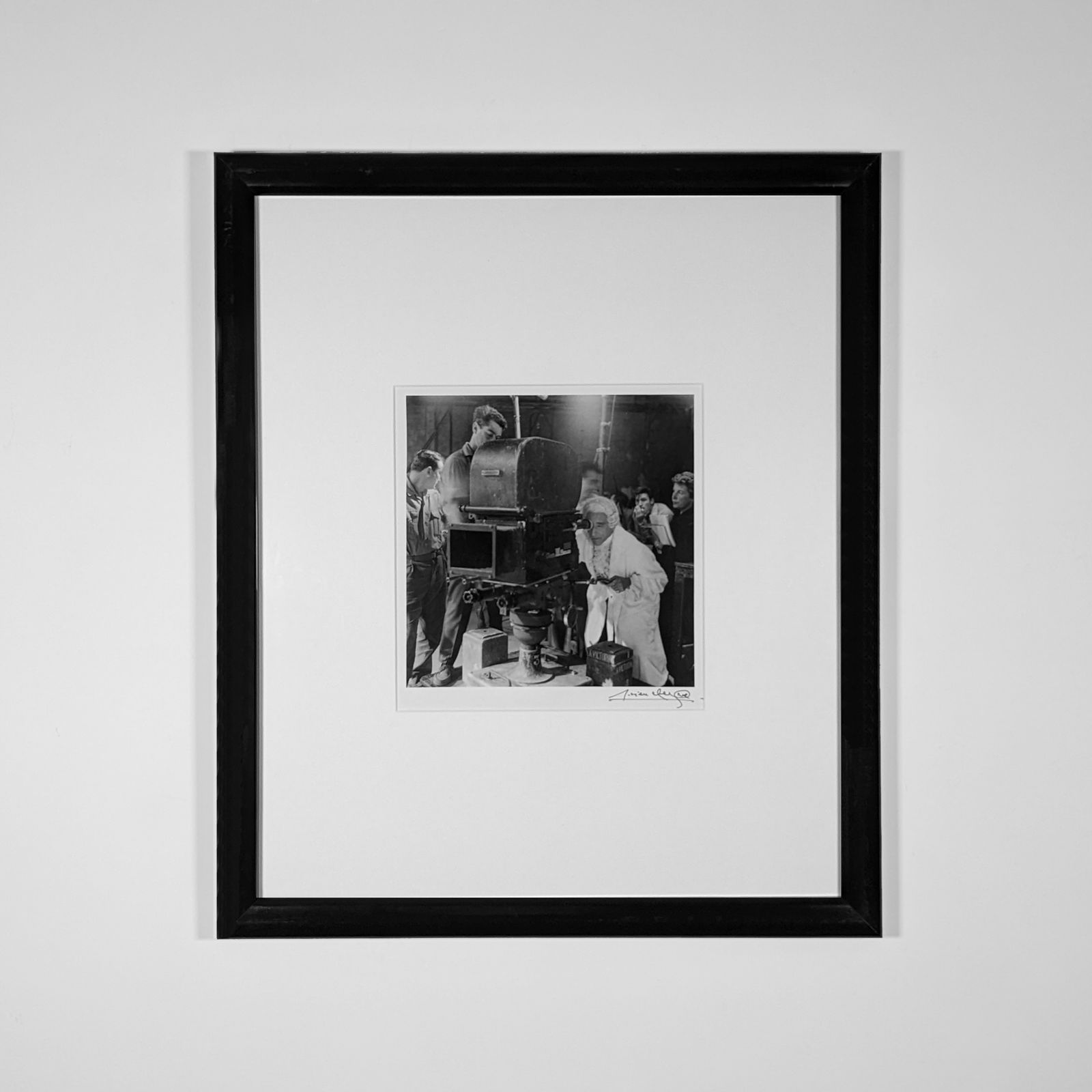 Framed Black and white photograph of Jean Cocteau in an 18th-century nobleman costume looking into a camera with members of the film crew looking behind him