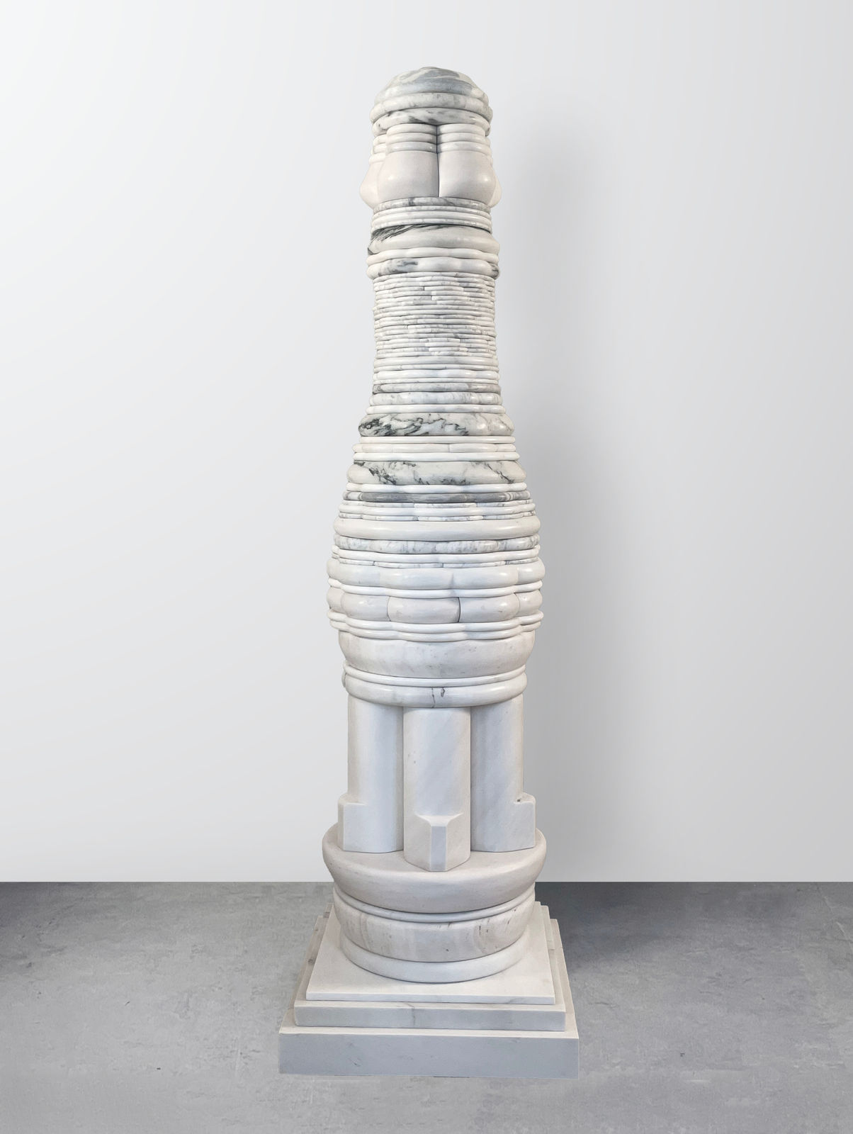 Human-scale totemic sculpture comprising layers of light-colored foliated marble