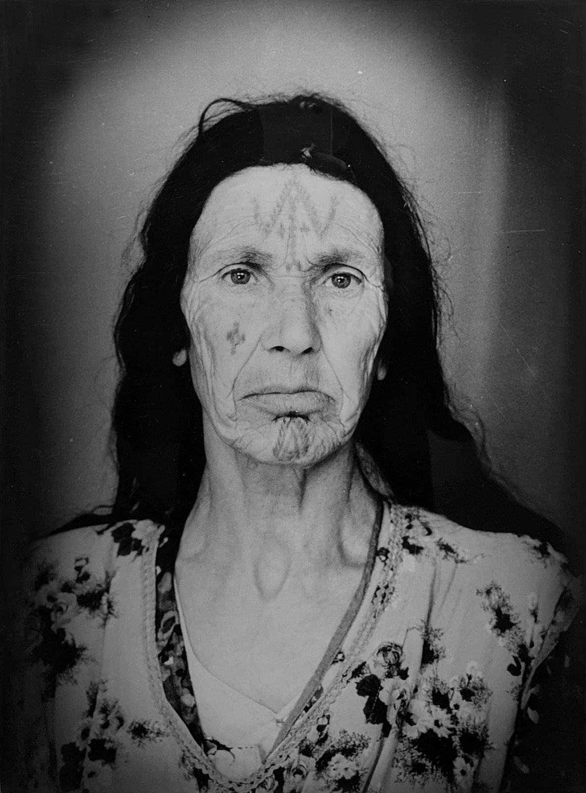 1960s black & white portrait of Amazigh woman with facial tattoos, wearing flowered dress, in a photography studio